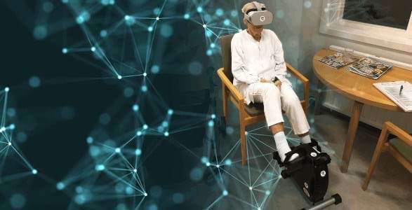 Ældre kvinde sidder i stole med VR-briller på og cykler på en sofacykel