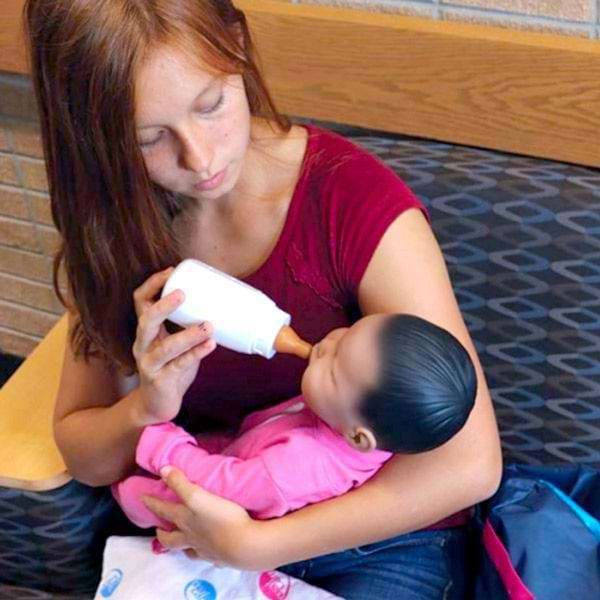 Ung kvinde giver sutteflaske til babysimulator